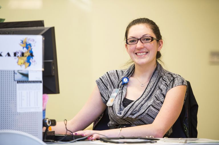 Woman sitting at a computer wearing glasses and smiling.