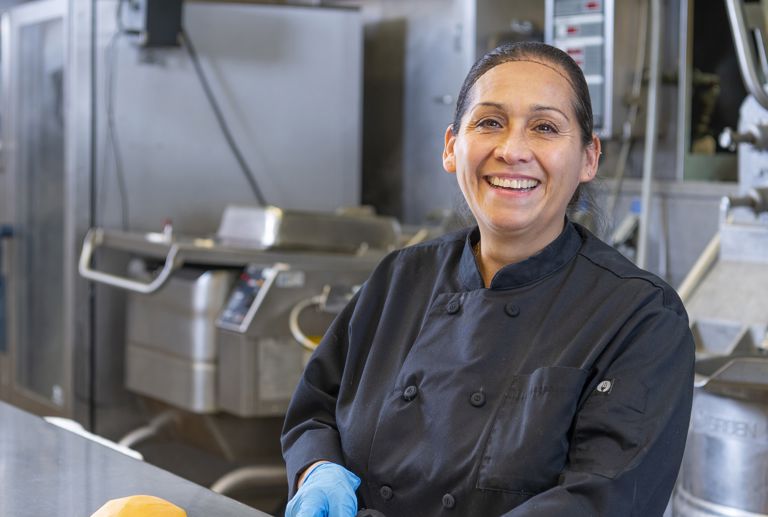 Woman chopping squash in a commercial kitchen and smiling.