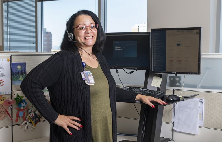 Woman standing at her office standing desk wearing a headset and smiling.