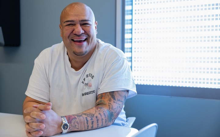 Man sitting at a break room table with his hands clasped on the table smiling. 