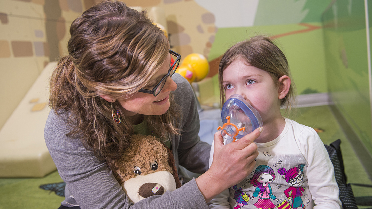 Child life specialist putting an anesthesia mask on patient to show her how it works