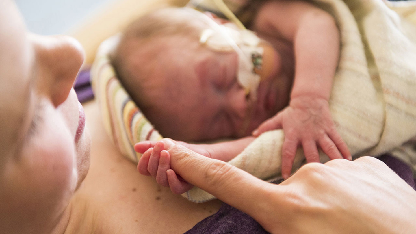 A close-up of a baby holding mom's finger.