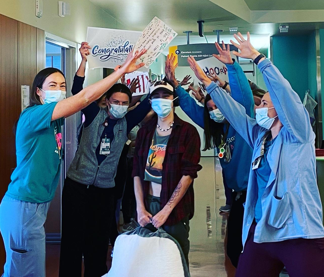 Seth stands under a human tunnel made by providers as some hold up signs congratulating him on discharge from the hospital.