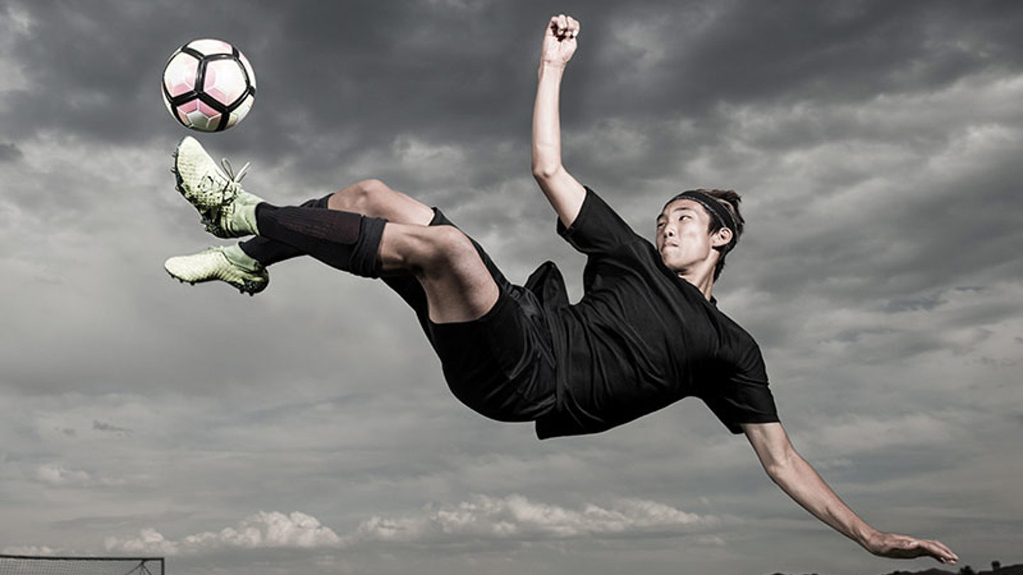 A teenage soccer player kicks the ball sideways in the air.